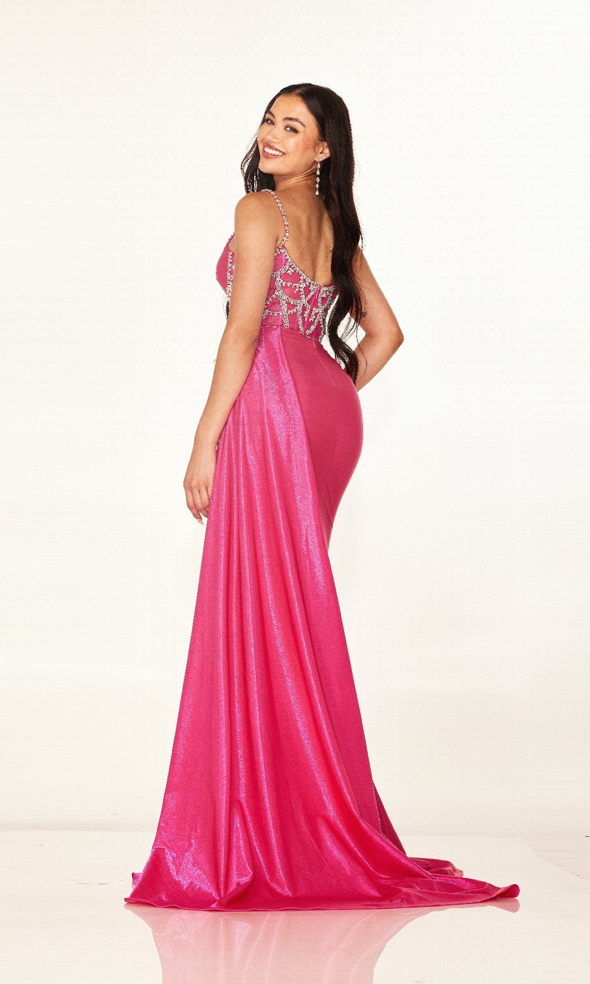 A woman stands and smiles in the Cecilia Couture 2628 long prom dress with a beaded bodice, facing backwards and looking over her shoulder against a plain light background.